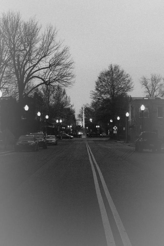 Empty road at dusk lined with lamps, black and white