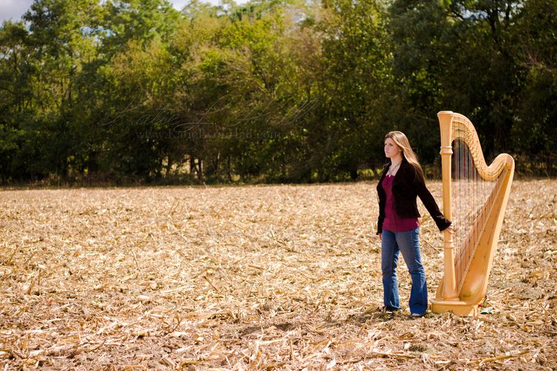 Harpist standing with her harp in an autumn harvested field
