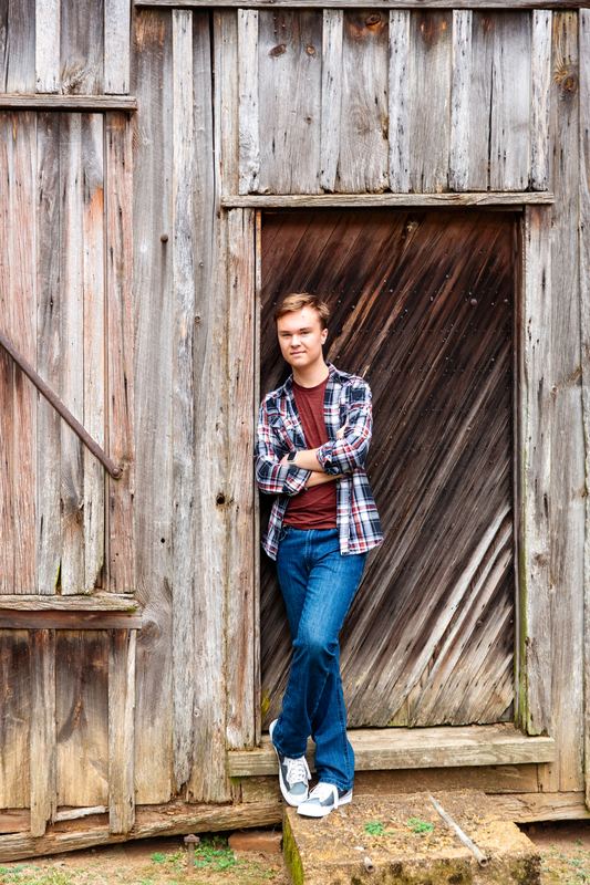 Young man in flannel leaning in the doorway of a weathered barn