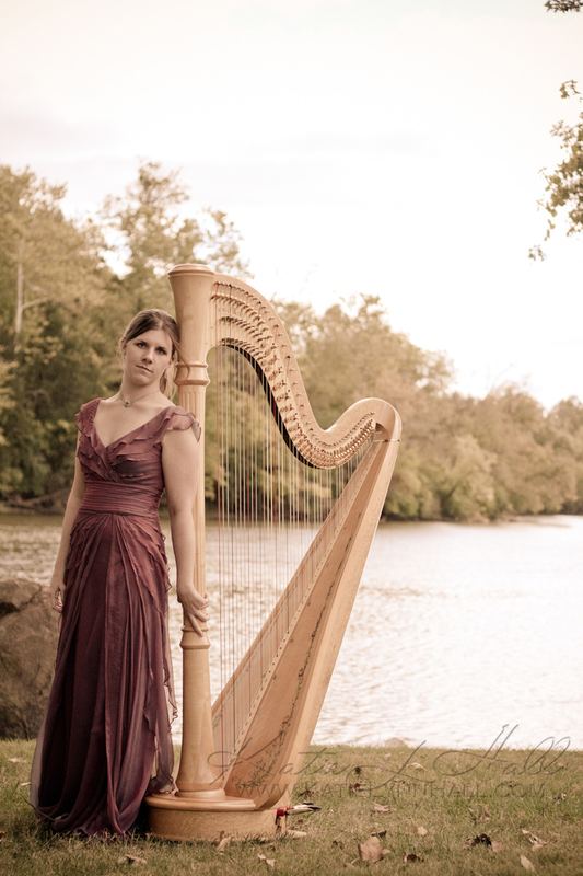 Harpist in a long gown with a golden harp at the river’s edge