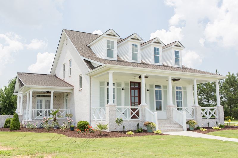 White farmhouse with a deep front porch and dormers under blue sky