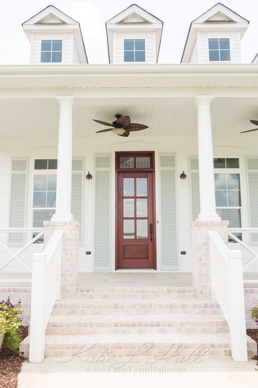 Front entry of a white farmhouse with a wooden door and porch fans