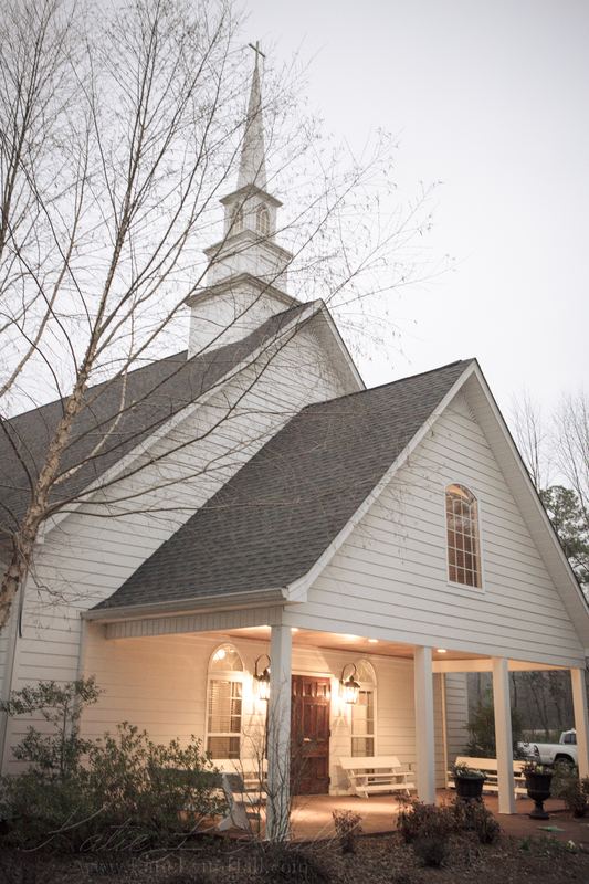 White chapel with a steeple and lit porch at dusk