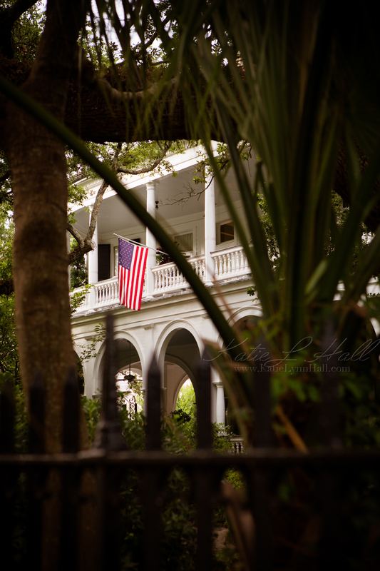 Historic columned home with an American flag seen through palms